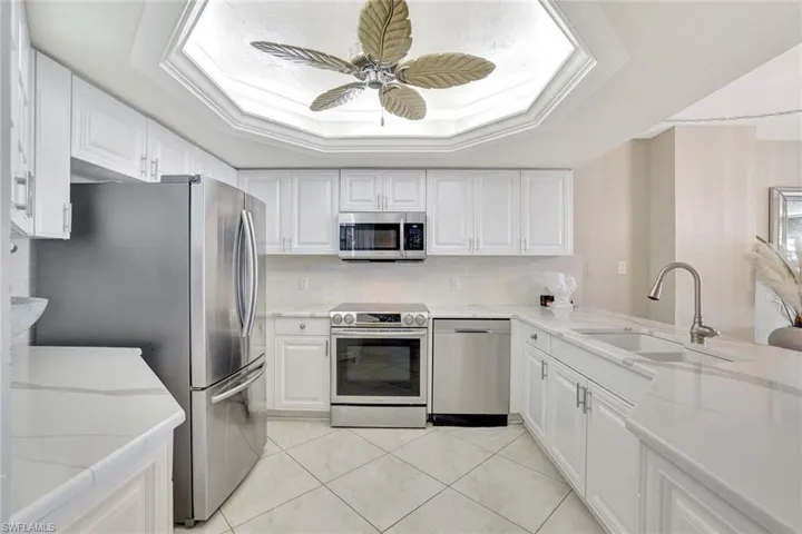 Kitchen with stainless steel appliances, light stone counters, white cabinets, a ceiling fan, and a tray ceiling