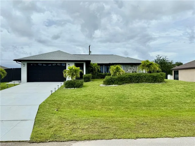 Ranch-style house featuring a garage, concrete driveway, a front yard, and a shingled roof