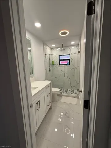 Bathroom featuring light marble finish flooring, a marble finish shower, vanity, and recessed lighting