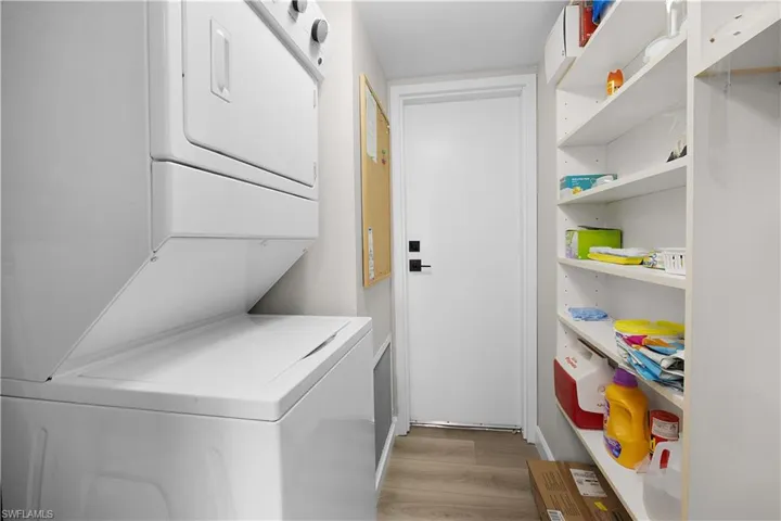 Dedicated utility area featuring a stacked laundry system, white interior door with matte black hardware, light wood-finish flooring, and built-in shelving