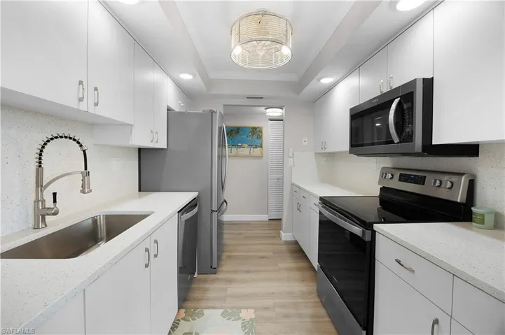 Galley kitchen featuring white cabinetry, light-toned countertops, and wood-finish flooring