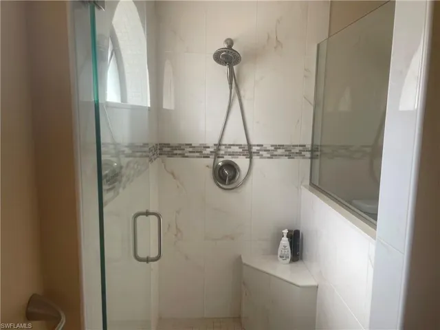 Glass-enclosed shower with white tiled walls, a decorative mosaic tile band, a built-in shower bench, and a brushed nickel shower fixture