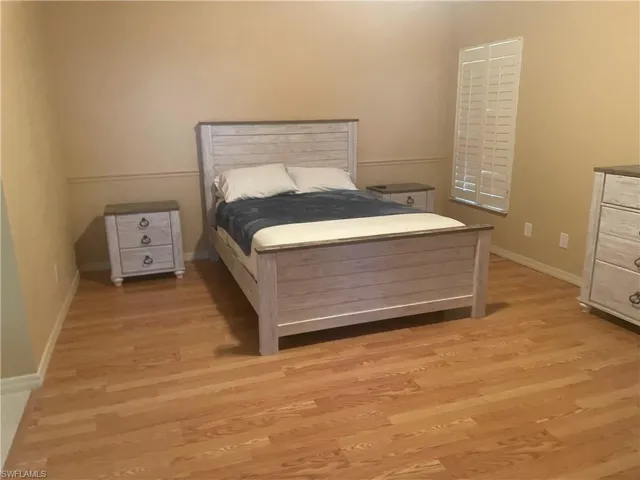 Spacious room featuring wood-finish flooring, neutral wall tones, and a window with plantation shutters