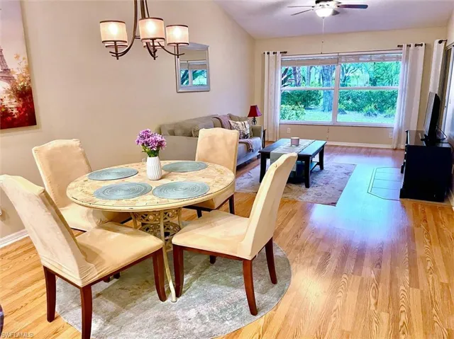 Open-concept living and dining area featuring wood-finish flooring, a vaulted ceiling, a large picture window, and a ceiling fan