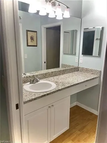 Bathroom vanity featuring a speckled countertop, integrated sink with chrome faucet, full-width mirror, and wood-finish flooring