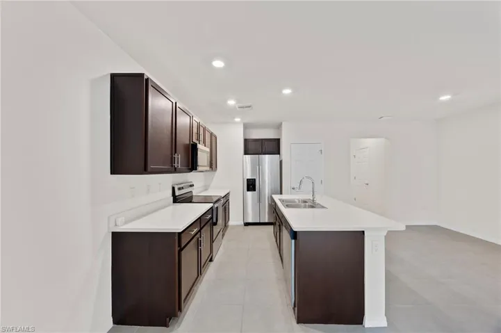 Kitchen featuring dark brown cabinetry, appliances with stainless steel finishes, light countertops, an island with sink, and recessed lighting