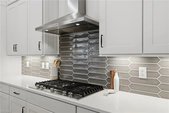 Kitchen with white cabinetry, stainless steel gas stovetop, decorative backsplash, and light stone counters
