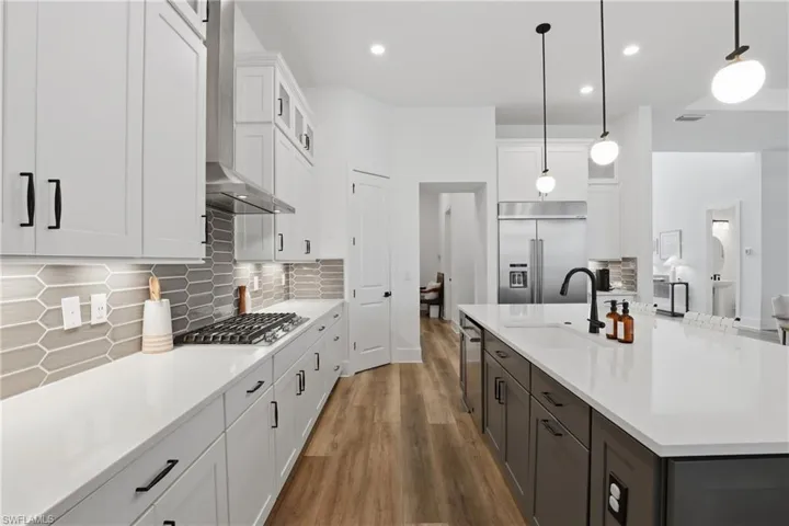 Two tone kitchen with dual tone cabinetry, dark wood-type flooring, glass insert cabinets, decorative backsplash, and stainless steel appliances