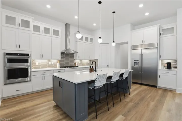 Kitchen with glass insert cabinets, backsplash, two tone color scheme, a kitchen breakfast bar, and stainless steel appliances