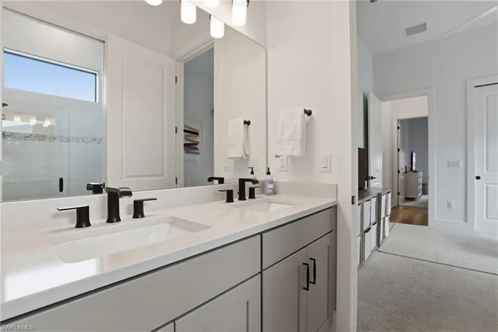 Full bathroom with double vanity, light colored carpet, and a shower stall