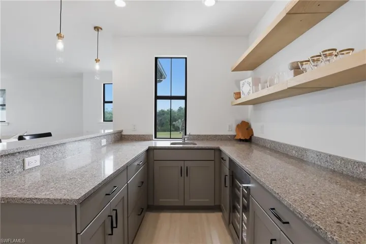 Kitchen featuring gray cabinetry, a peninsula, pendant lighting, beverage cooler, and light stone counters
