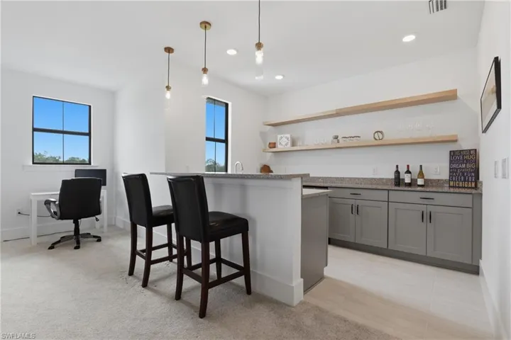 Kitchen featuring light stone countertops, a breakfast bar, gray cabinets, a center island with sink, and hanging light fixtures