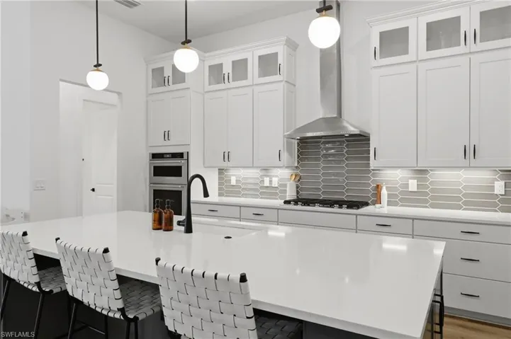 Kitchen with a kitchen breakfast bar, glass fronted cabinets, pendant lighting, and white cabinets