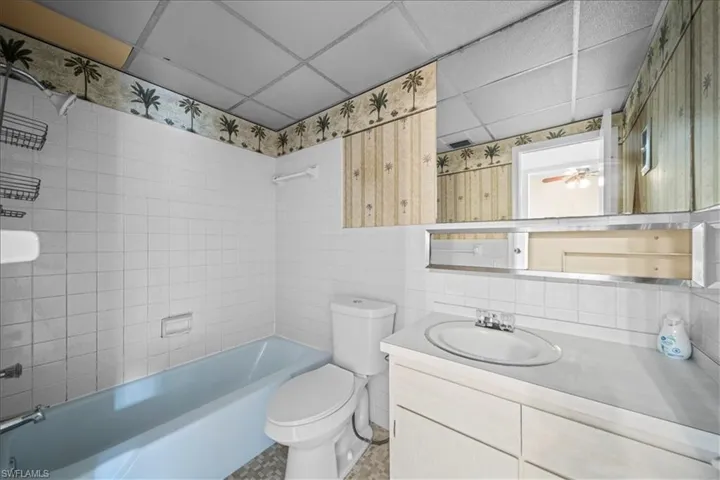 Full bath with  shower combination, a drop ceiling, vanity, tile walls, and backsplash