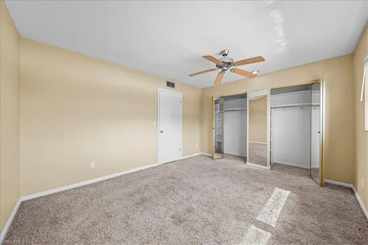 Unfurnished bedroom featuring carpet floors, multiple closets, a textured ceiling, and ceiling fan