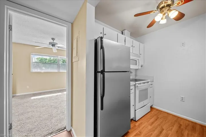 Kitchen featuring a ceiling fan, white appliances, light countertops, white cabinets, and light wood-style flooring