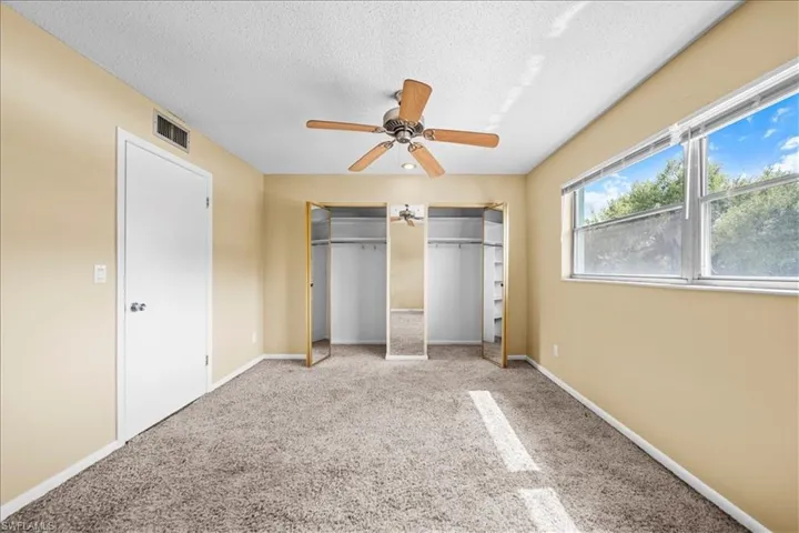 Unfurnished bedroom with two closets, carpet flooring, a textured ceiling, and a ceiling fan