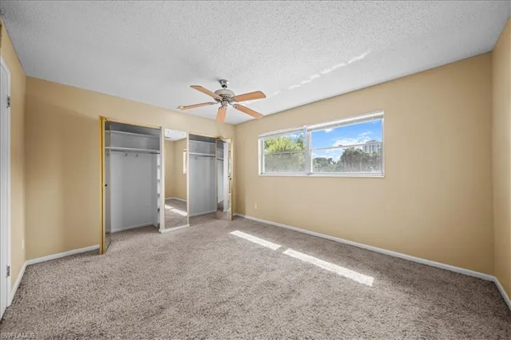 Unfurnished bedroom with two closets, carpet flooring, a ceiling fan, and a textured ceiling
