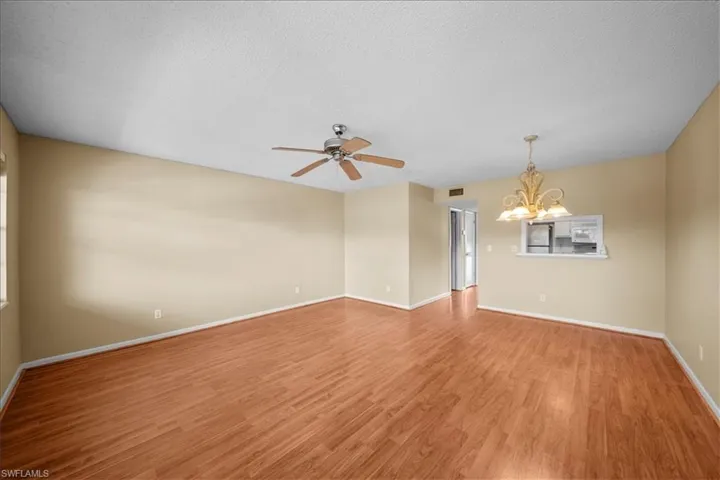 Empty room featuring a textured ceiling, light wood finished floors, a chandelier, and a ceiling fan