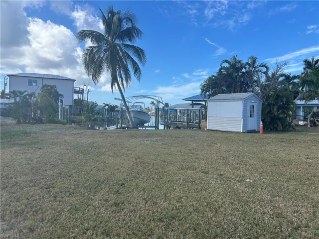 View of grassy yard featuring boat lift, a boat dock, and a storage unit