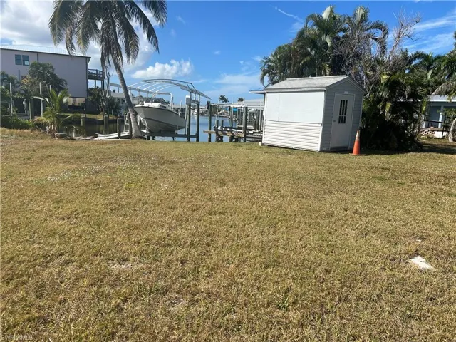 View of green lawn featuring boat lift, a dock, a water view, and an outbuilding
