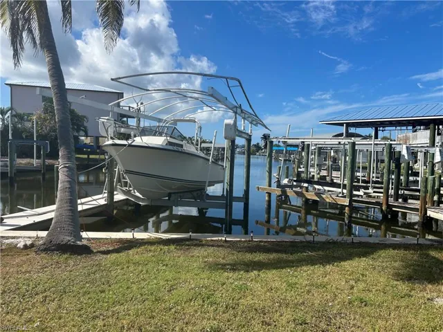 Dock featuring boat lift, a lawn, and a water view