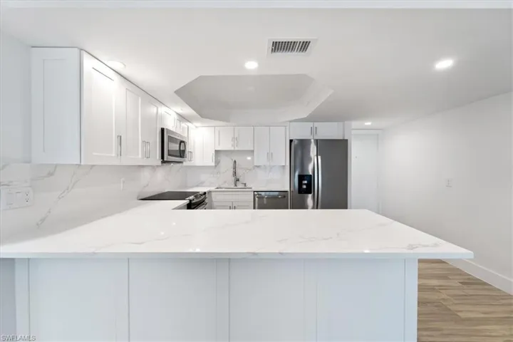 100 Estero BLVD #633_Kitchen with appliances with stainless steel finishes, a sink, a peninsula, a tray ceiling, and light stone countertops