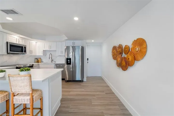 100 Estero BLVD #633_Virtually Staged -Kitchen with appliances with stainless steel finishes, a kitchen breakfast bar, baseboards, white cabinets, and light wood finished floors