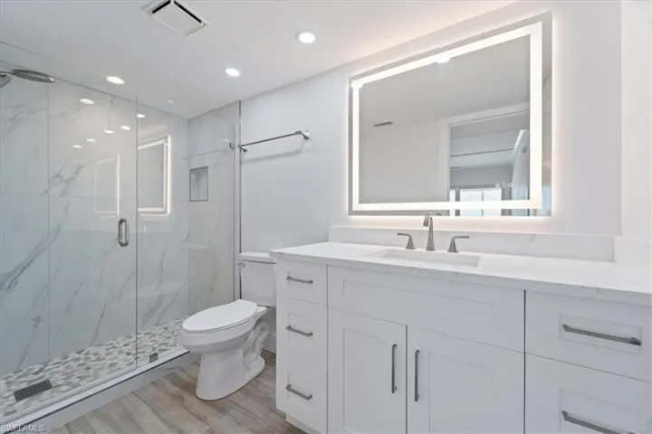 100 Estero BLVD #633_Bathroom with toilet, a marble finish shower, wood finished floors, vanity, and recessed lighting