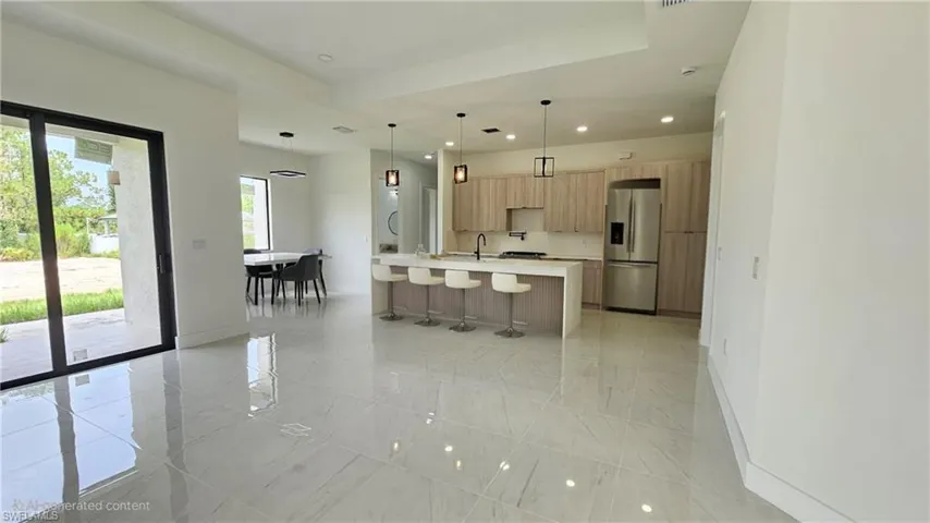 Kitchen with recessed lighting, decorative light fixtures, a kitchen bar, stainless steel fridge, and a center island with sink