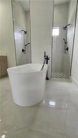 Bathroom featuring a walk in shower, a soaking tub, and light marble finish floors