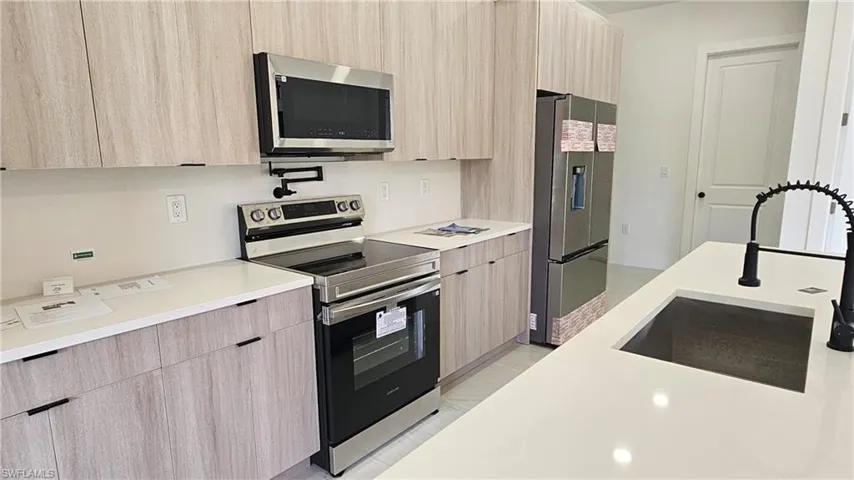 Kitchen with modern cabinets, light brown cabinetry, stainless steel appliances, and light tile patterned floors