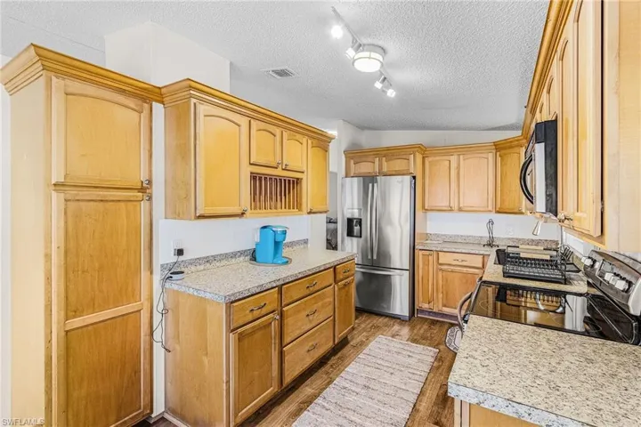 Kitchen featuring stainless steel fridge, black range with electric stovetop, dark wood-style floors, a textured ceiling, and light countertops
