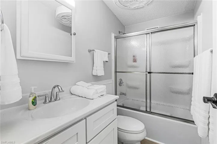 Bathroom with vanity, a textured ceiling, and bath / shower combo with glass door