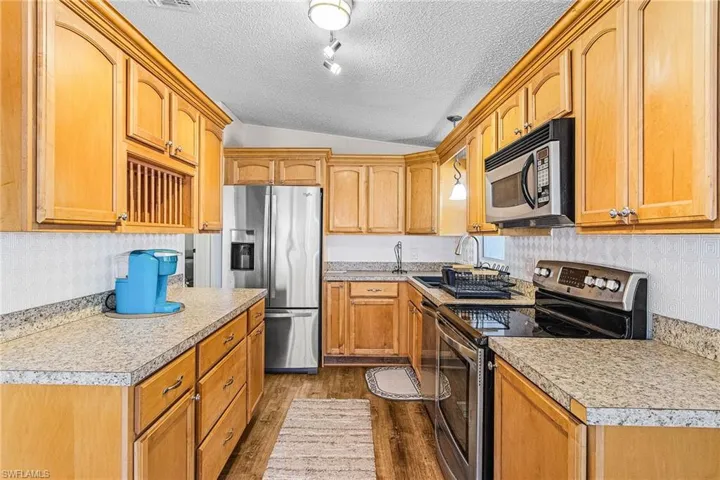 Kitchen with stainless steel appliances, vaulted ceiling, dark wood-style flooring, a textured ceiling, and light countertops