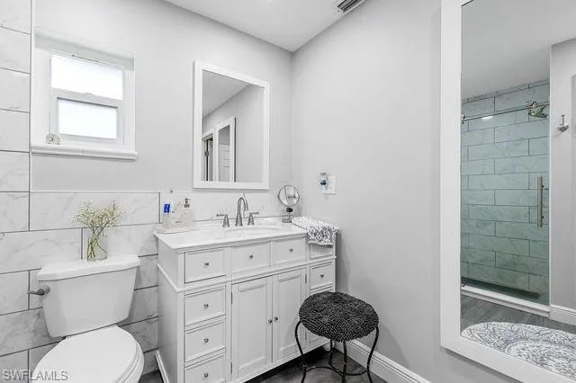 Bathroom featuring tile walls, tiled shower, toilet, and vanity