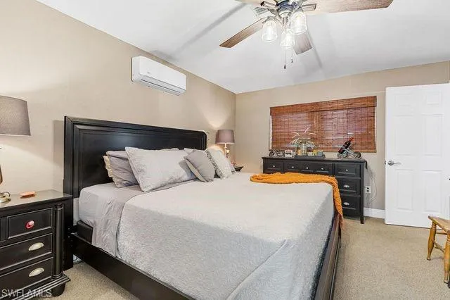 Carpeted bedroom with a wall unit AC and ceiling fan