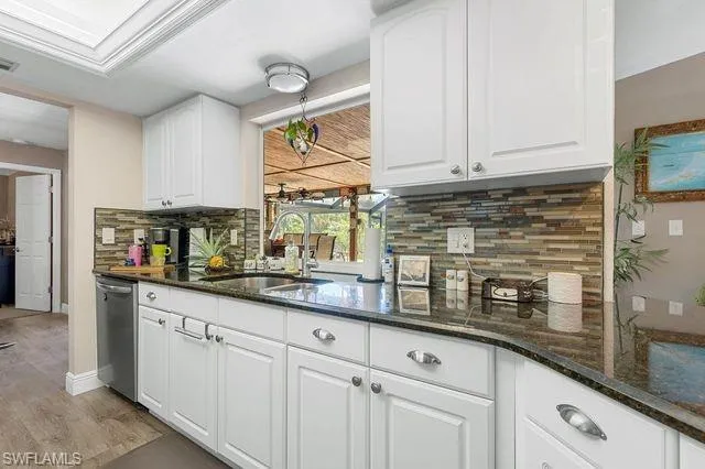 Kitchen with stainless steel dishwasher, light wood-type flooring, backsplash, sink, and white cabinets