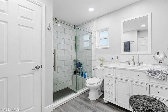 Bathroom with an enclosed shower, vanity, toilet, and hardwood / wood-style floors