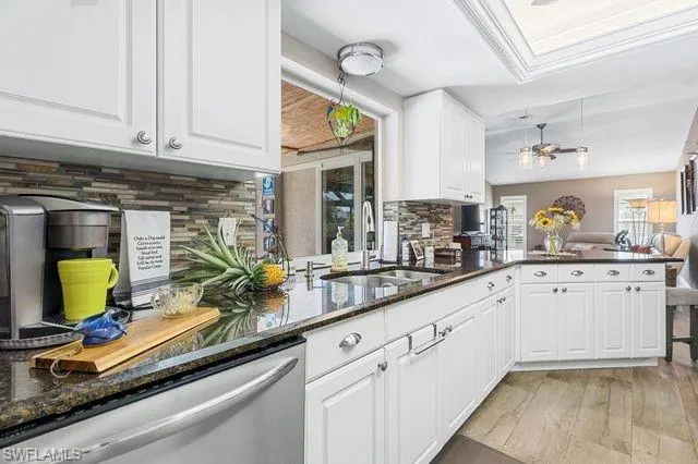 Kitchen with light hardwood / wood-style floors, tasteful backsplash, stainless steel dishwasher, sink, and white cabinetry