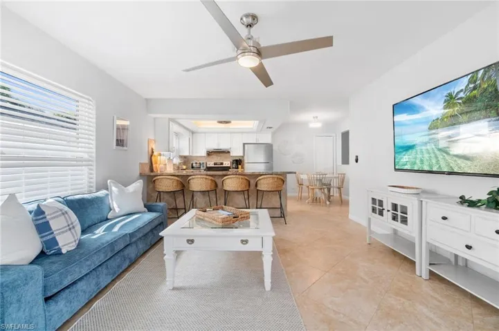 Living room with light tile patterned floors, a tray ceiling, and ceiling fan