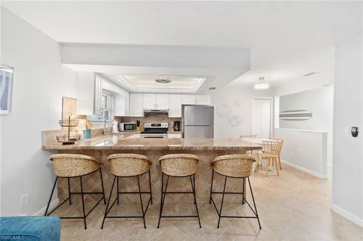 Kitchen with kitchen peninsula, white cabinets, a kitchen breakfast bar, a tray ceiling, and stainless steel appliances