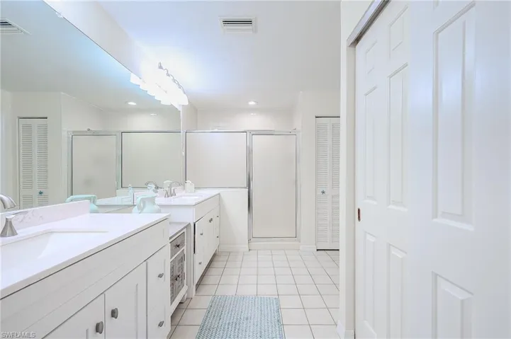 Bathroom with a closet, two vanities, a stall shower, and light tile patterned floors