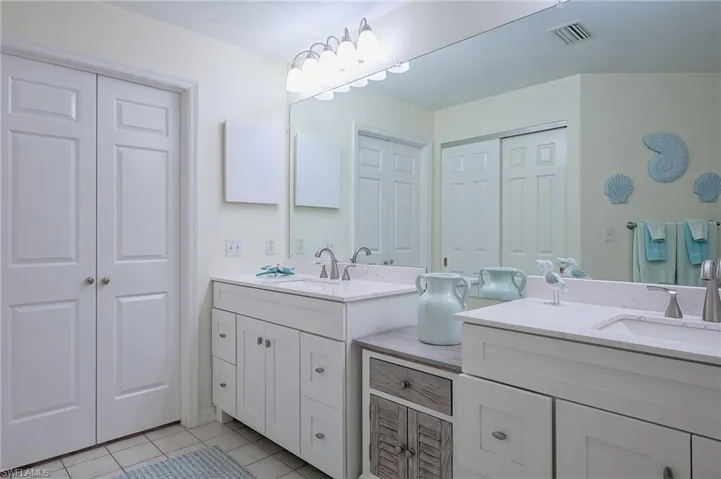 Full bath with a closet, light tile patterned floors, and two vanities