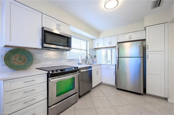 Kitchen featuring appliances with stainless steel finishes, white cabinets, backsplash, and light stone counters