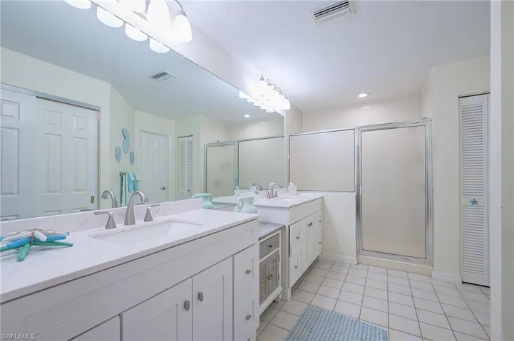 Bathroom featuring a closet, two vanities, a shower stall, and light tile patterned flooring
