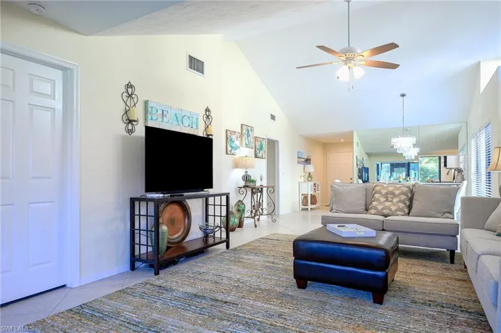 Living room with light tile patterned floors, a chandelier, a ceiling fan, and high vaulted ceiling