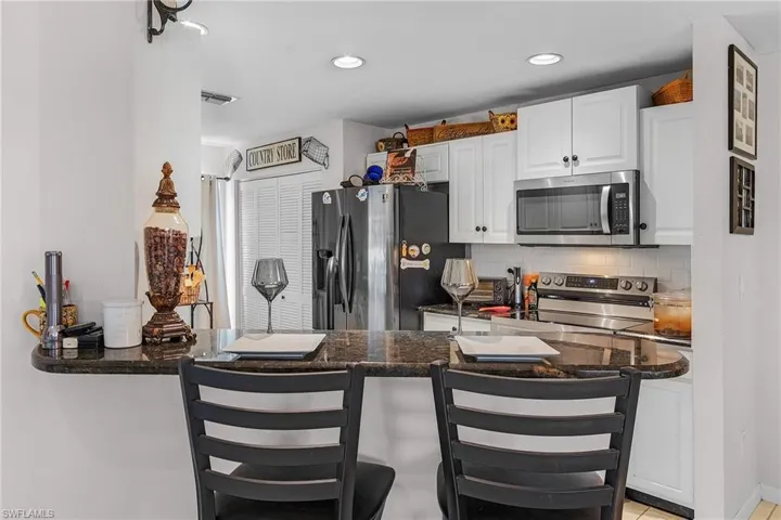 Kitchen with backsplash, appliances with stainless steel finishes, white cabinetry, and a breakfast bar area