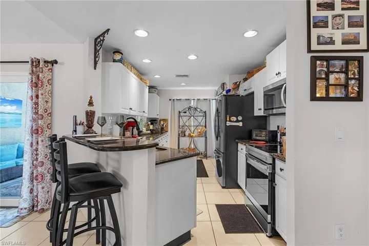 Kitchen featuring a peninsula, appliances with stainless steel finishes, a breakfast bar area, white cabinets, and light tile patterned floors