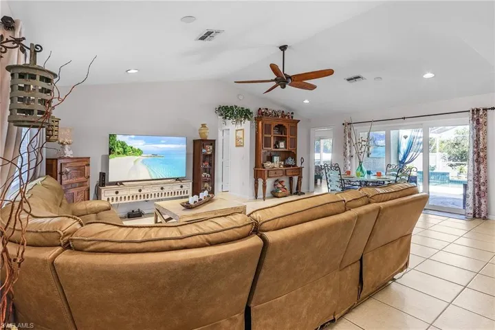 Living area with light tile patterned floors, visible vents, ceiling fan, and vaulted ceiling